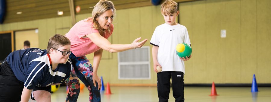 Übungsleiterin mit 2 Jungen in Turnhalle (Inklusion)