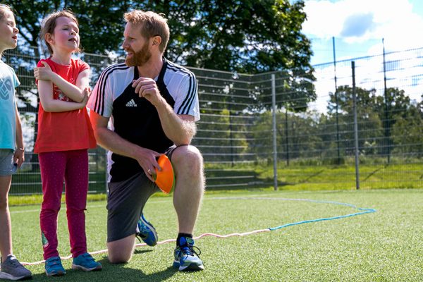 Übungsleiter draußen beim Training mit zwei Kindern 