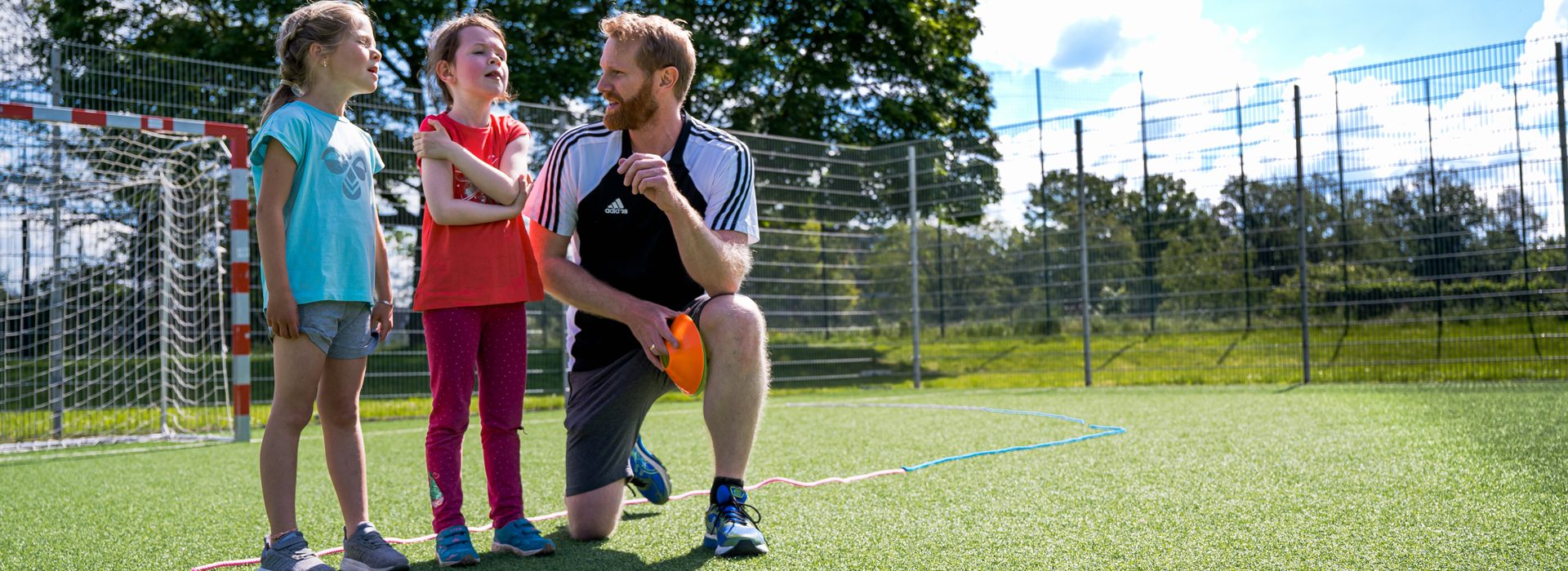 Übungsleiter mit zwei Kindern bei Sport draußen