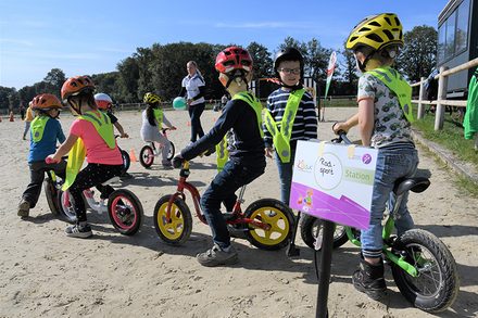 Bild: Mehrere Kinder auf Laufrädern. Sie tragen einen Helm und eine Warnweste.
