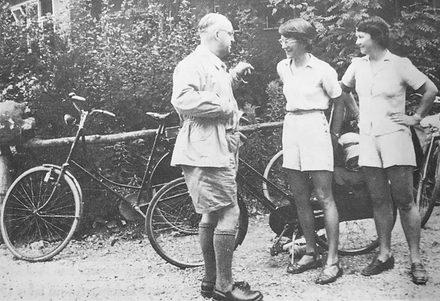 Bild: Im Vordergrund ist ein Mann sowie zwei Frauen zu sehen. Sie tragen sommerliche Kleidung und unterhalten sich. Im Hintergrund ist ein Fahrrad. 
